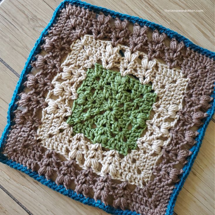 a crocheted square with a green center on a wooden surface, in the shape of a flower