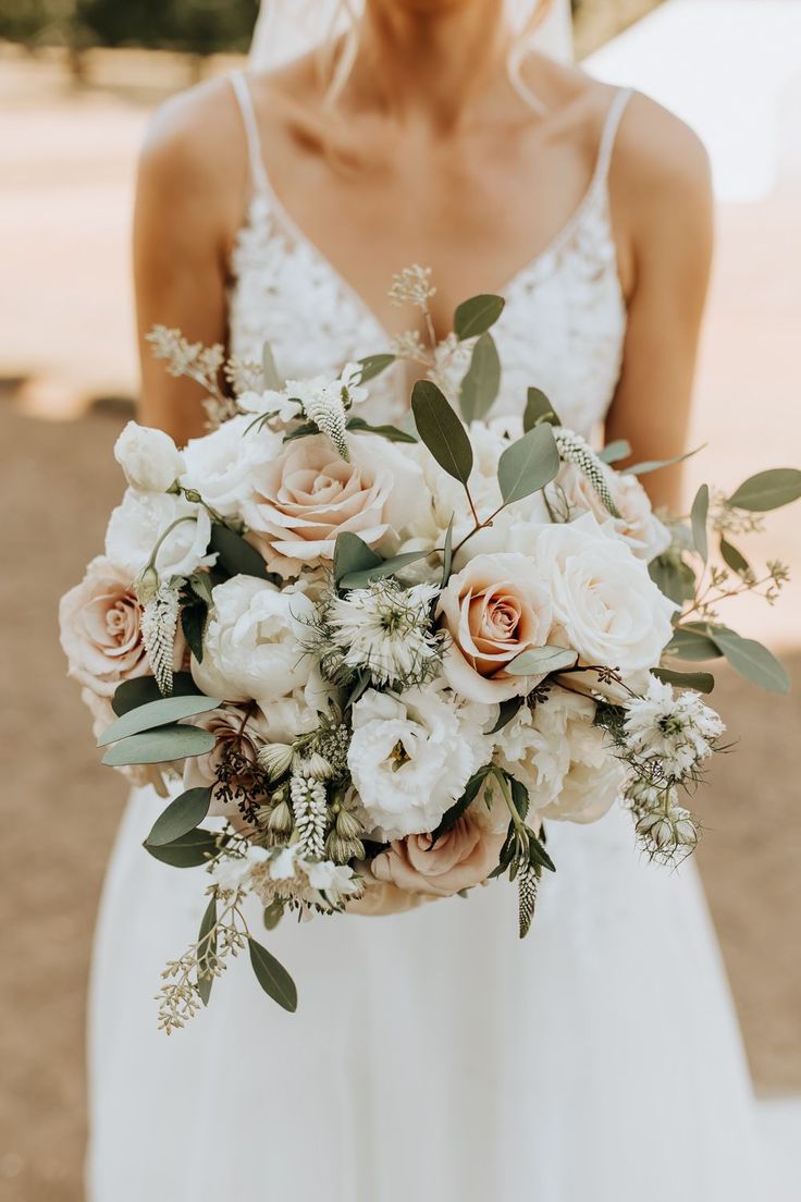 a woman holding a bouquet of flowers in her hands and wearing a wedding dress with straps