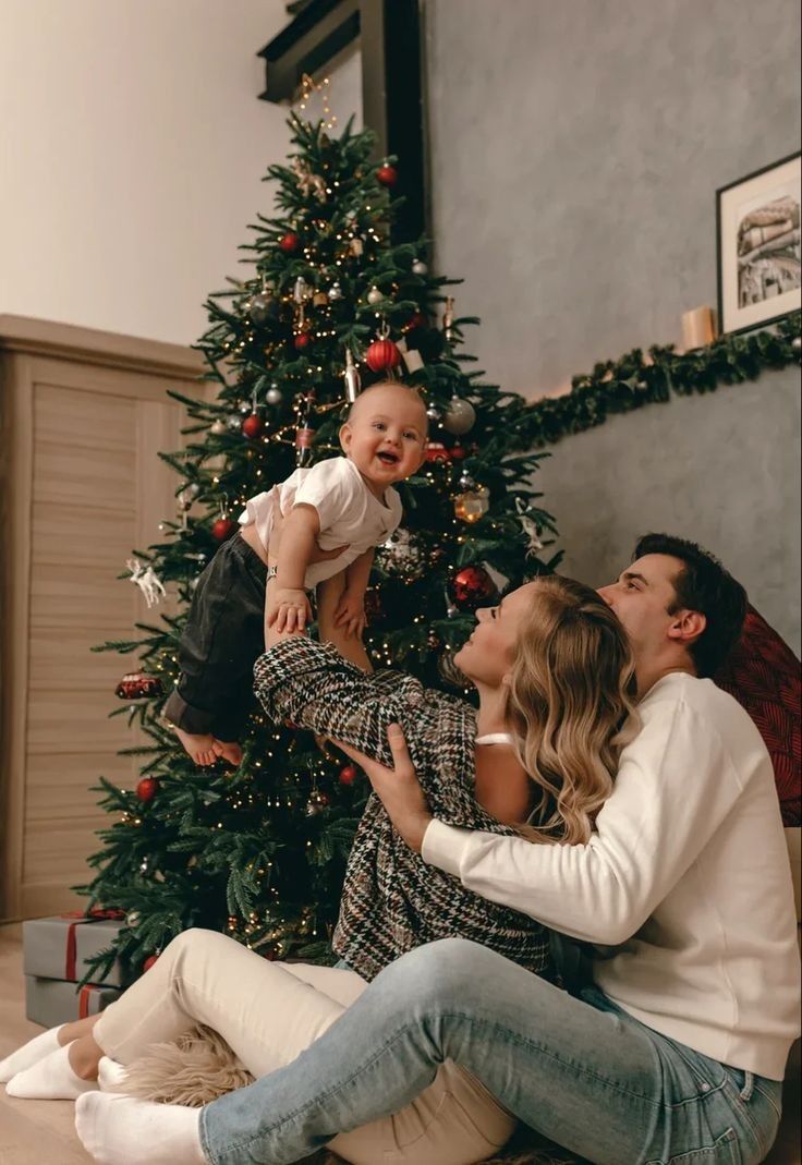 a family sitting on the floor in front of a christmas tree with their toddler