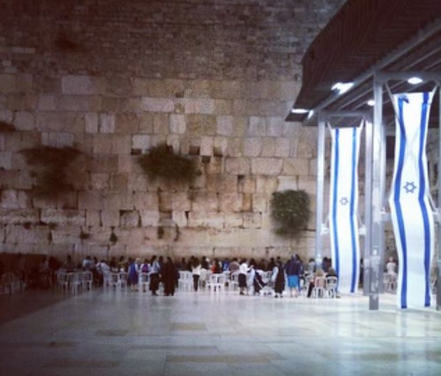 a group of people sitting at tables in front of a stone wall with blue and white columns