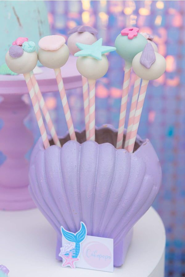 there are some little mermaid cupcakes in the shell with candy sticks sticking out of it