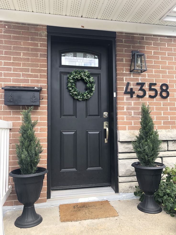 a black front door with two planters and a wreath on it