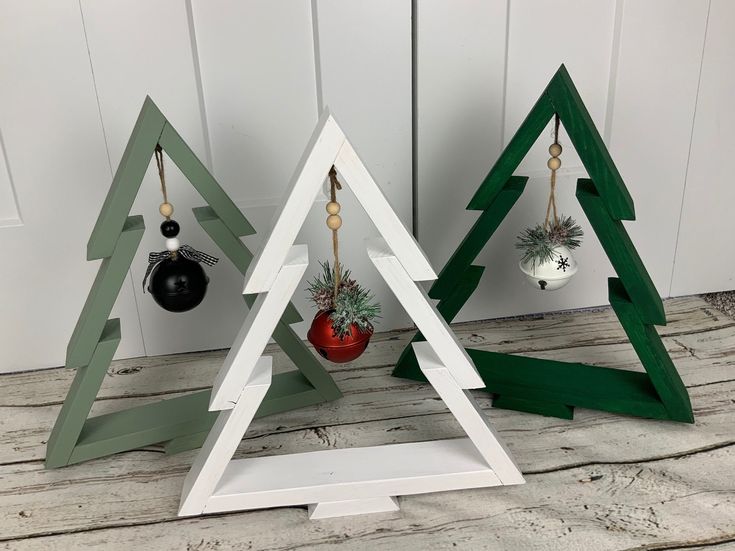 three wooden christmas trees with ornaments hanging from the top and bottom, on a wood floor