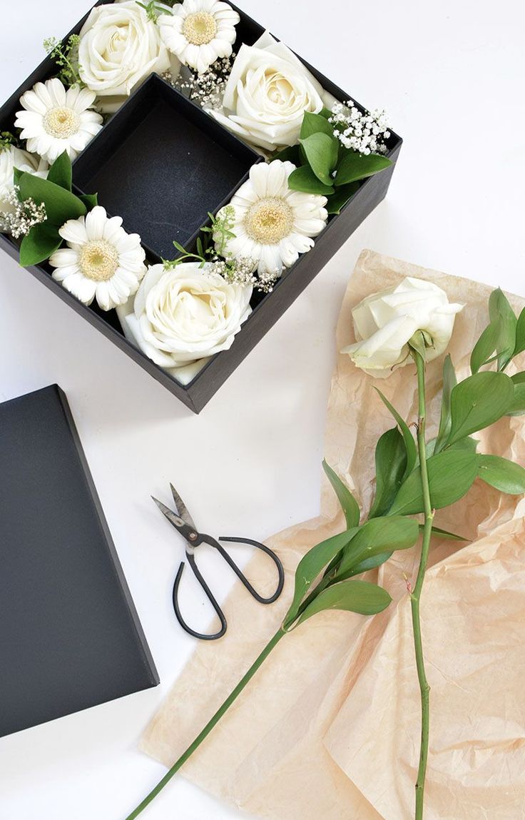 flowers and scissors are on the table next to a box with white roses in it