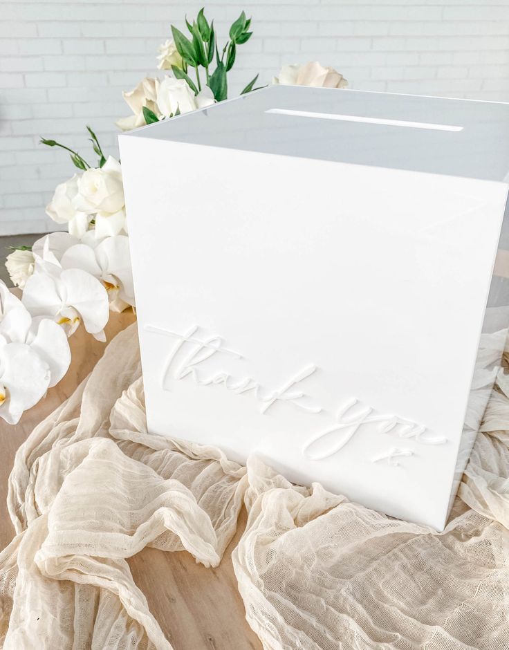 a white box sitting on top of a wooden table next to some flowers and cloth