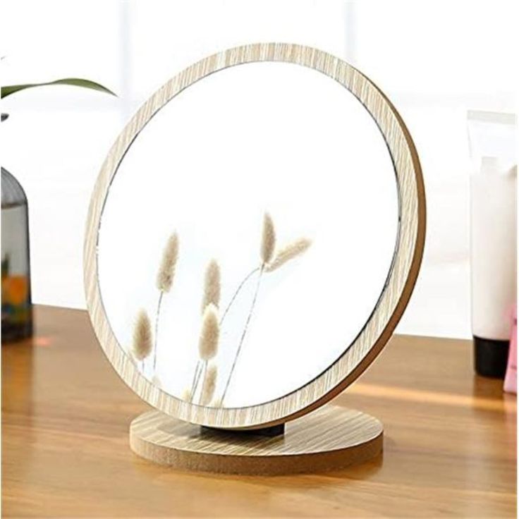 a mirror sitting on top of a wooden table next to a vase with flowers in it