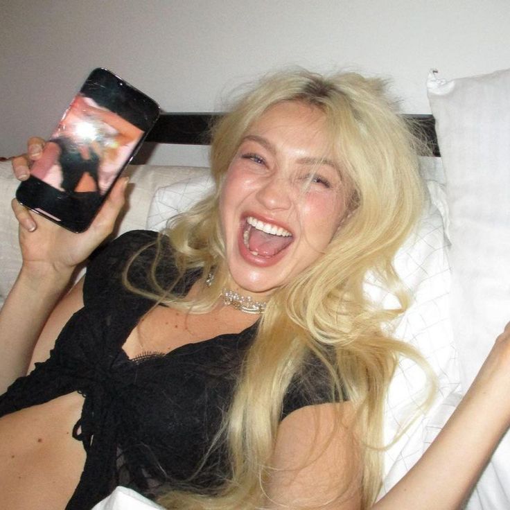 a woman laying in bed holding up a cell phone