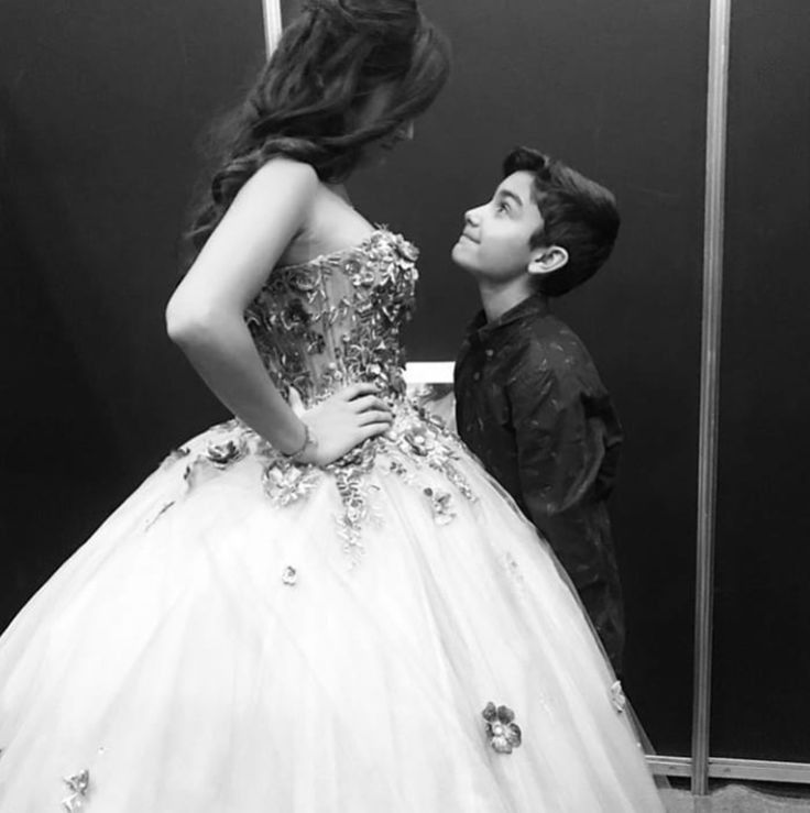 a young boy standing next to a woman in a ball gown and looking at her