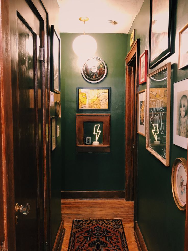 a hallway with green walls and pictures on the wall next to an area rug in front of two doorways