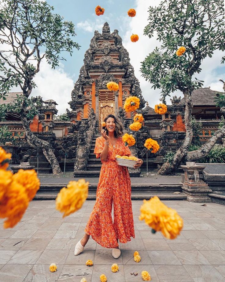 a woman standing in front of a temple surrounded by yellow flowers and orange pom poms