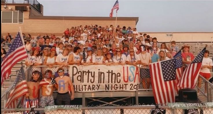 a group of people holding american flags in front of a fence with a party in the usa banner