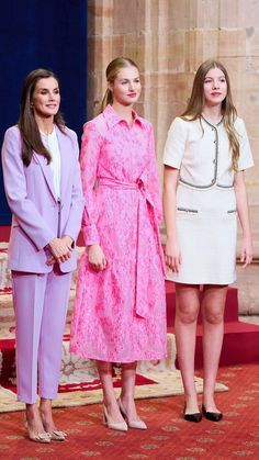 three women standing next to each other in front of a stage with red carpet and pillars