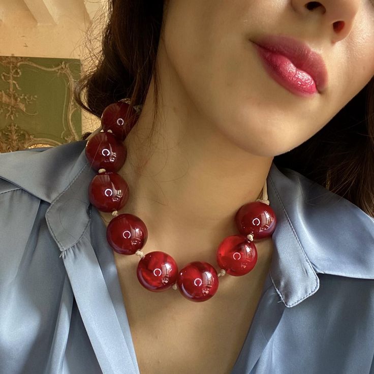 a woman wearing a blue shirt and red necklace with two buttons on it's collar