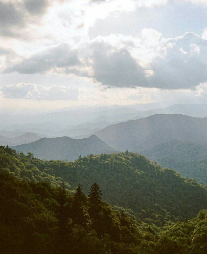 the mountains are covered in green trees and clouds