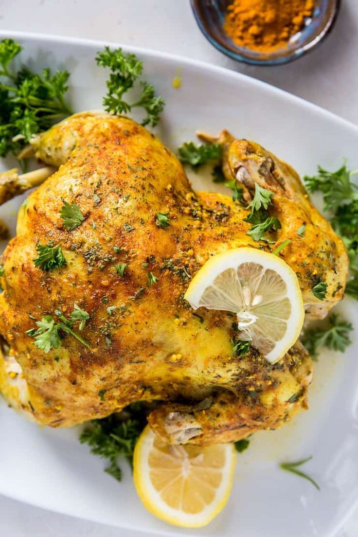 a white plate topped with a chicken covered in herbs and garnished with lemon wedges