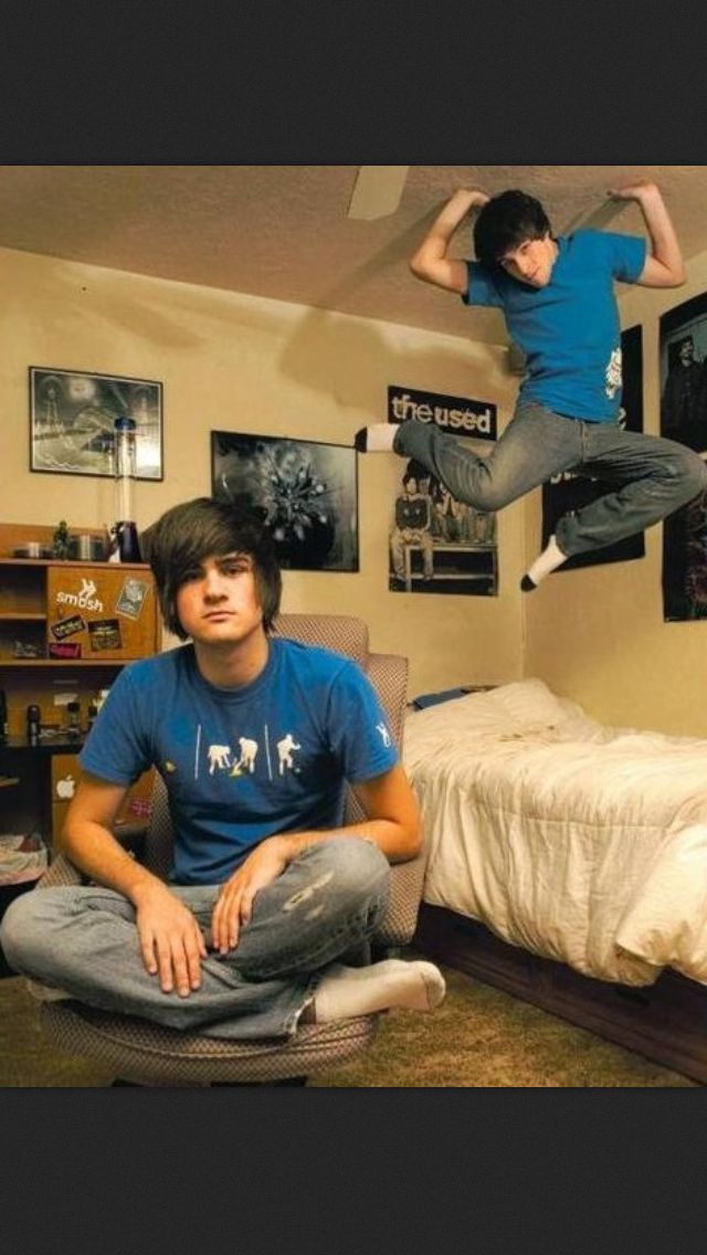 a young man is jumping in the air over his bed and another boy is sitting on an office chair