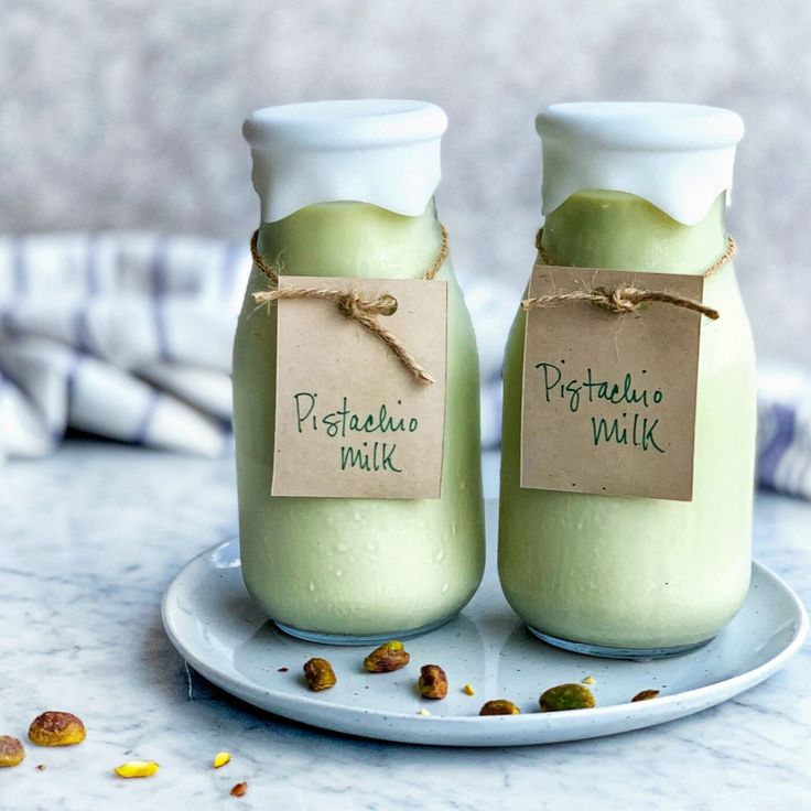 two jars filled with pistachio milk sitting on a plate next to each other