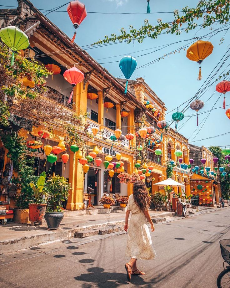 a woman is walking down the street in front of some buildings with lanterns hanging from it