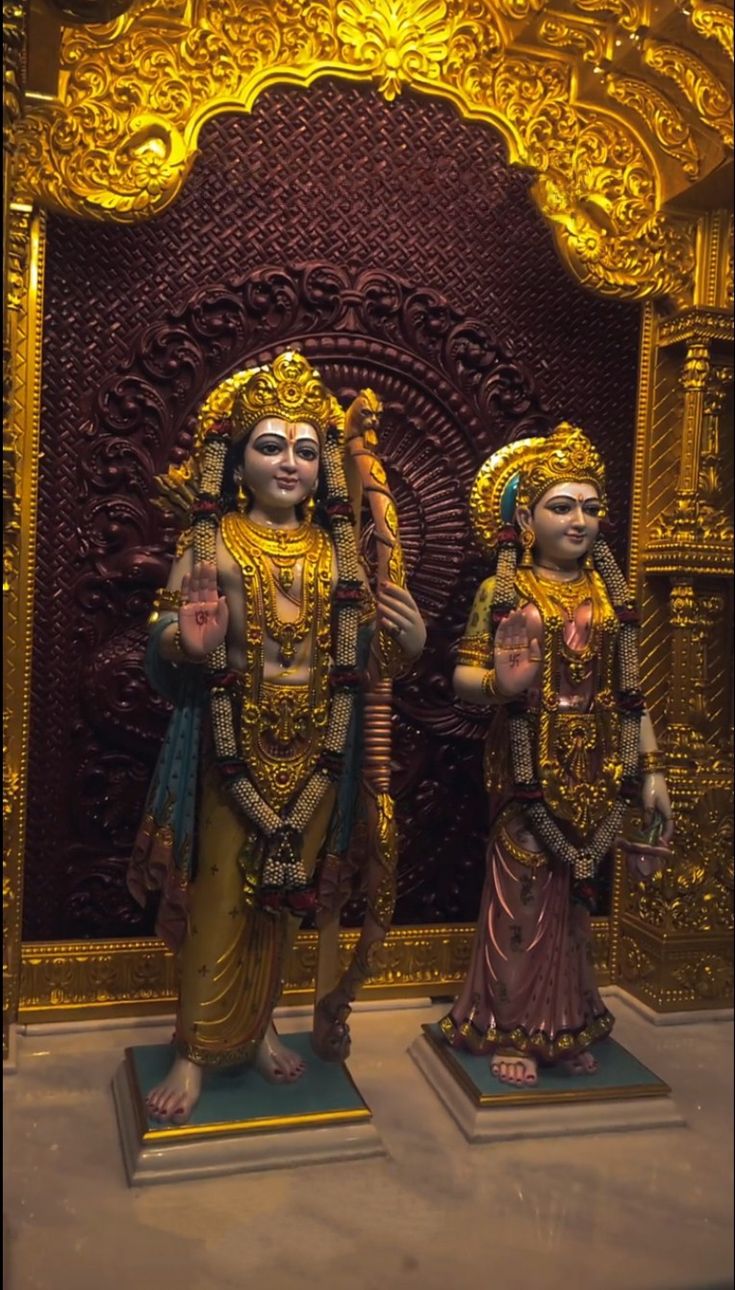 two statues of hindu deities standing in front of a golden wall with words above them