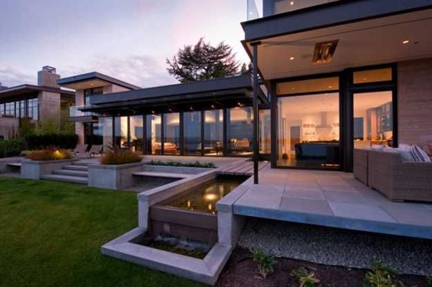 an outdoor living area with water feature and seating areas at dusk time, in front of a modern home