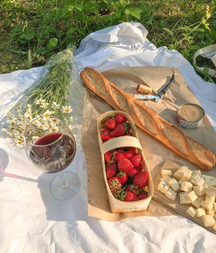 strawberries, cheese and bread on a picnic blanket with wine in the foreground