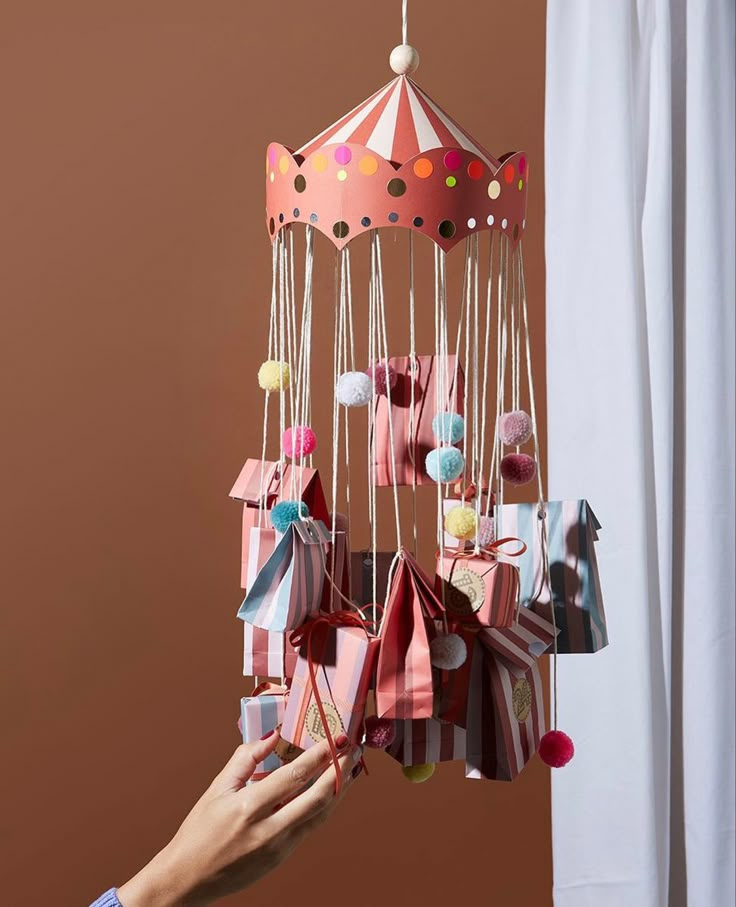 a person is holding an origami mobile in front of a curtain and window