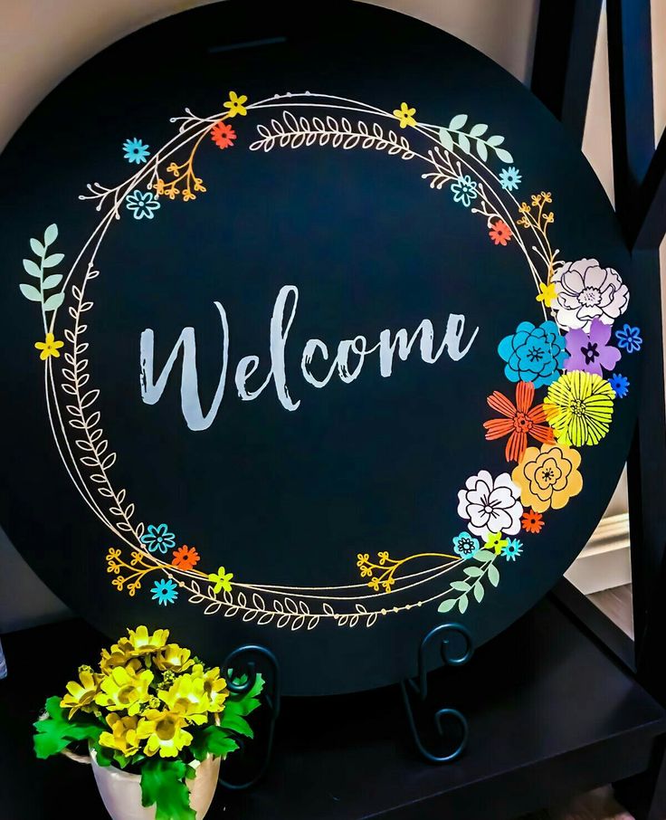 a welcome sign with flowers painted on it and a potted plant next to it