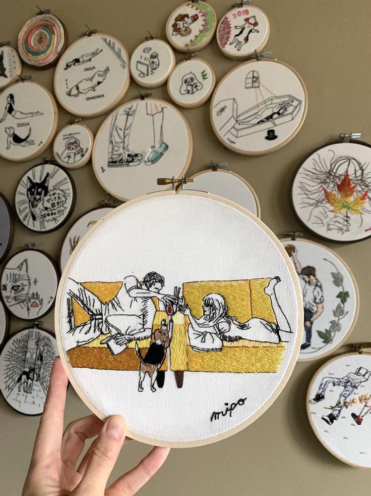 someone is holding up their embroidery work in front of the wall with many pictures on it