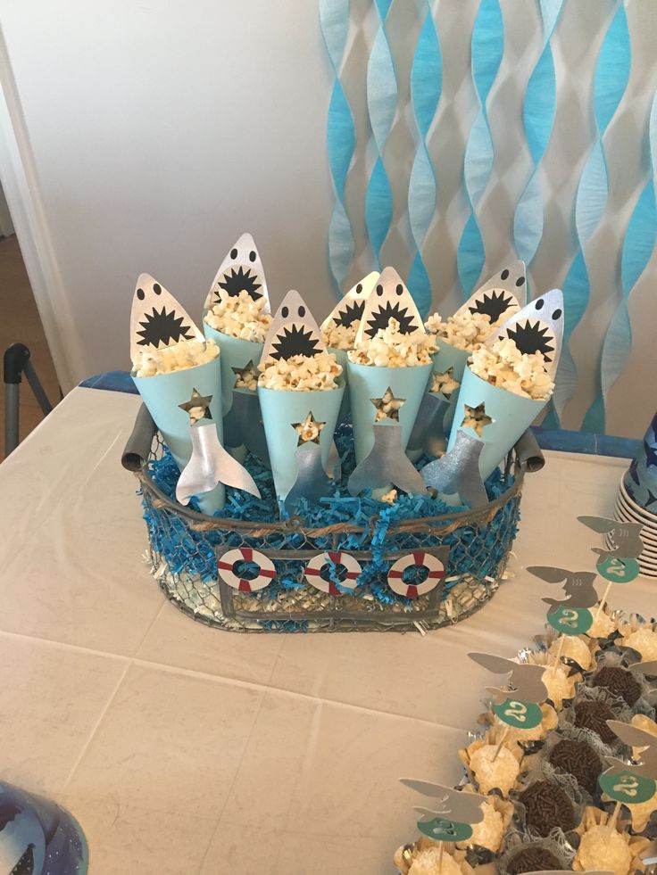 a table topped with cupcakes covered in blue frosting and shark fin decorations