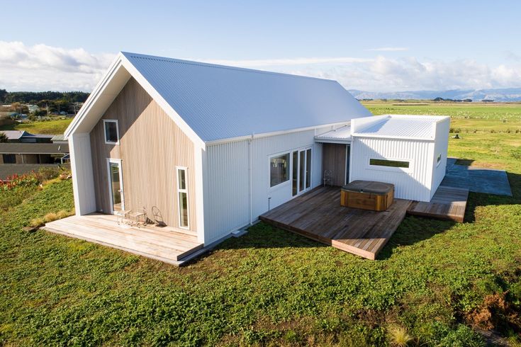 a small white house sitting on top of a lush green field next to a wooden deck