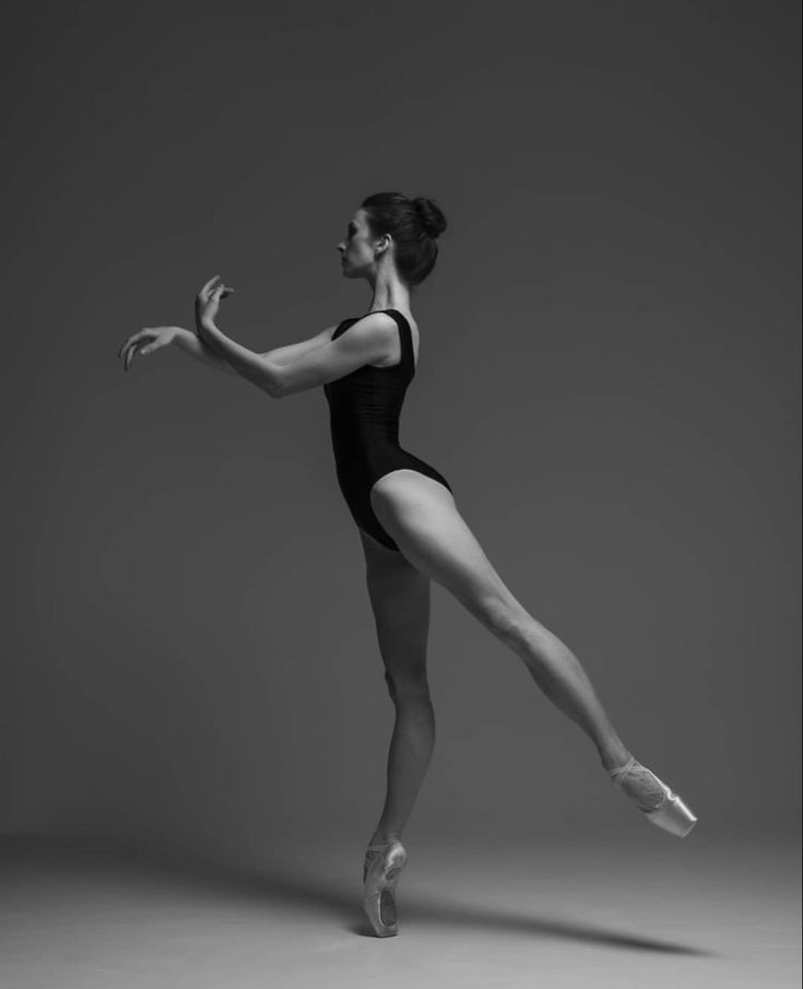 a woman in a black leotard and ballet shoes is standing on one leg