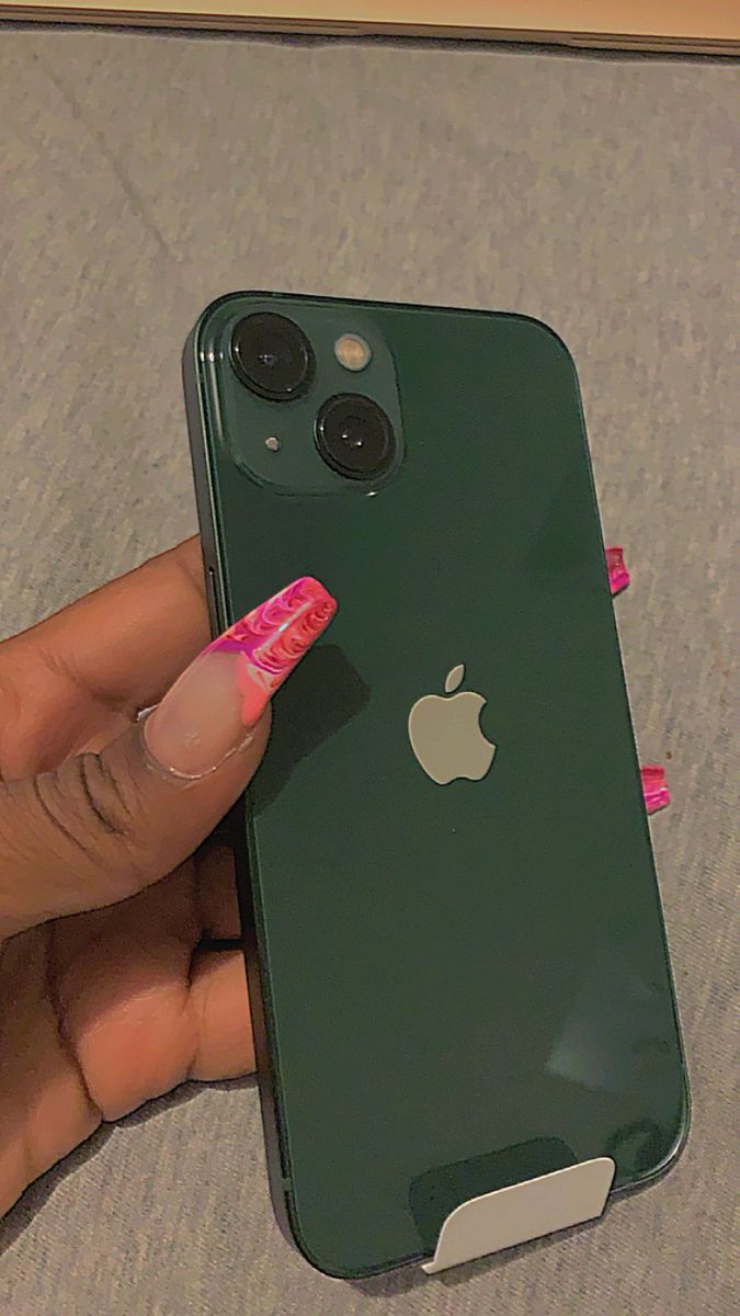 a woman's hand holding an iphone in front of the camera with pink nail polish