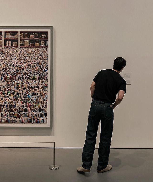 a man standing in front of a wall with many pictures on it and looking at the ground