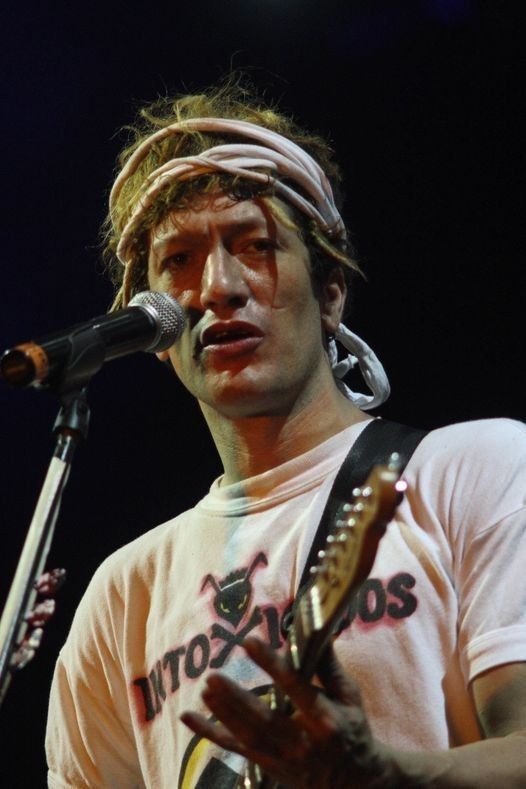 a man with dreadlocks on his head holding a guitar in front of a microphone