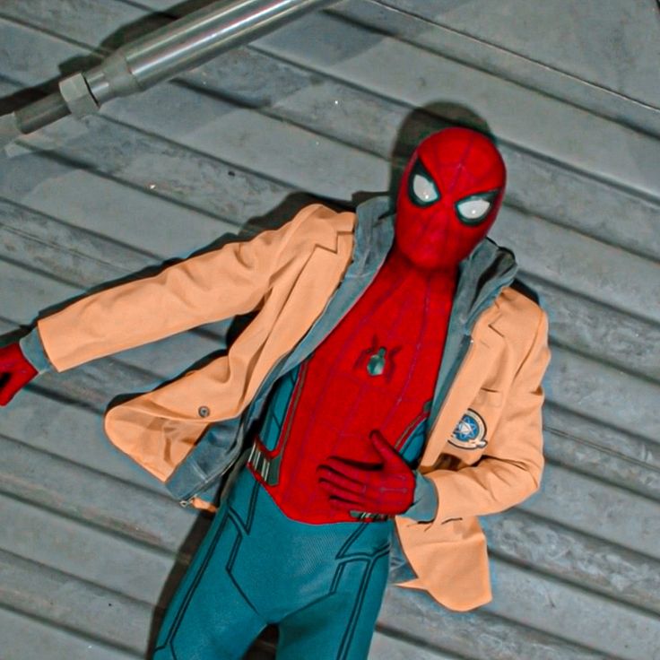 a man dressed as spider - man is standing in front of a metal wall with his hands on his hips