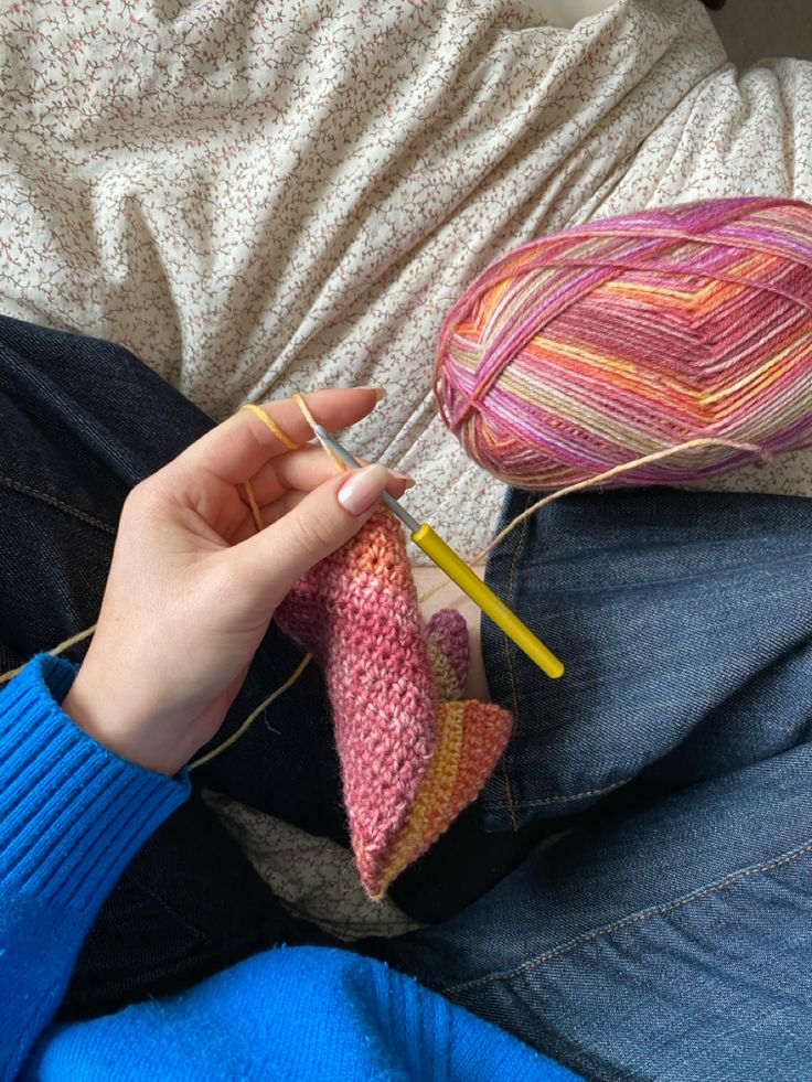 a person is knitting on the couch with yarn and crochet needles in their hands