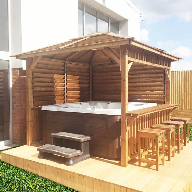 a hot tub sitting on top of a wooden deck next to a building and green grass