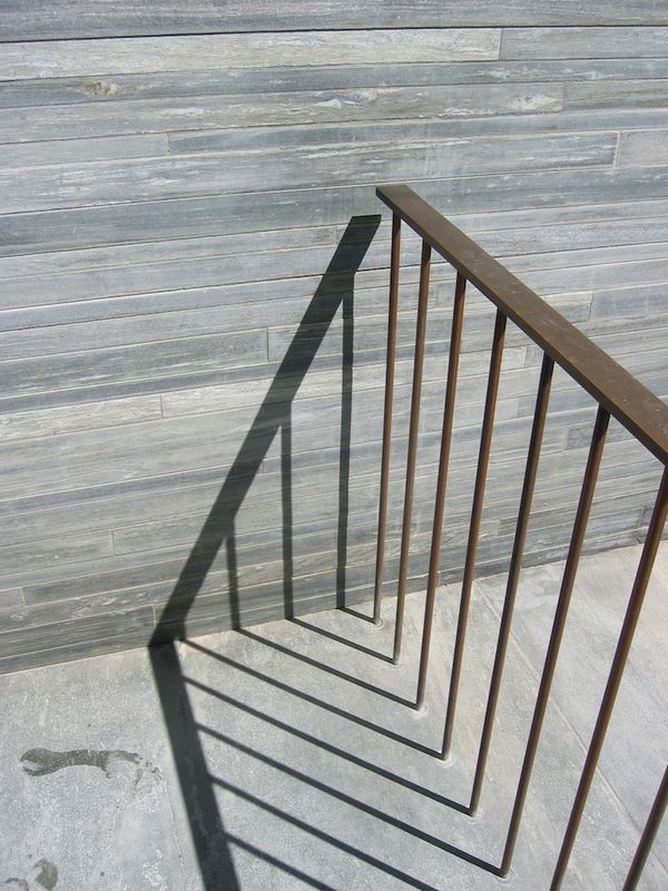 the shadow of an iron railing on a wooden wall next to a metal hand rail