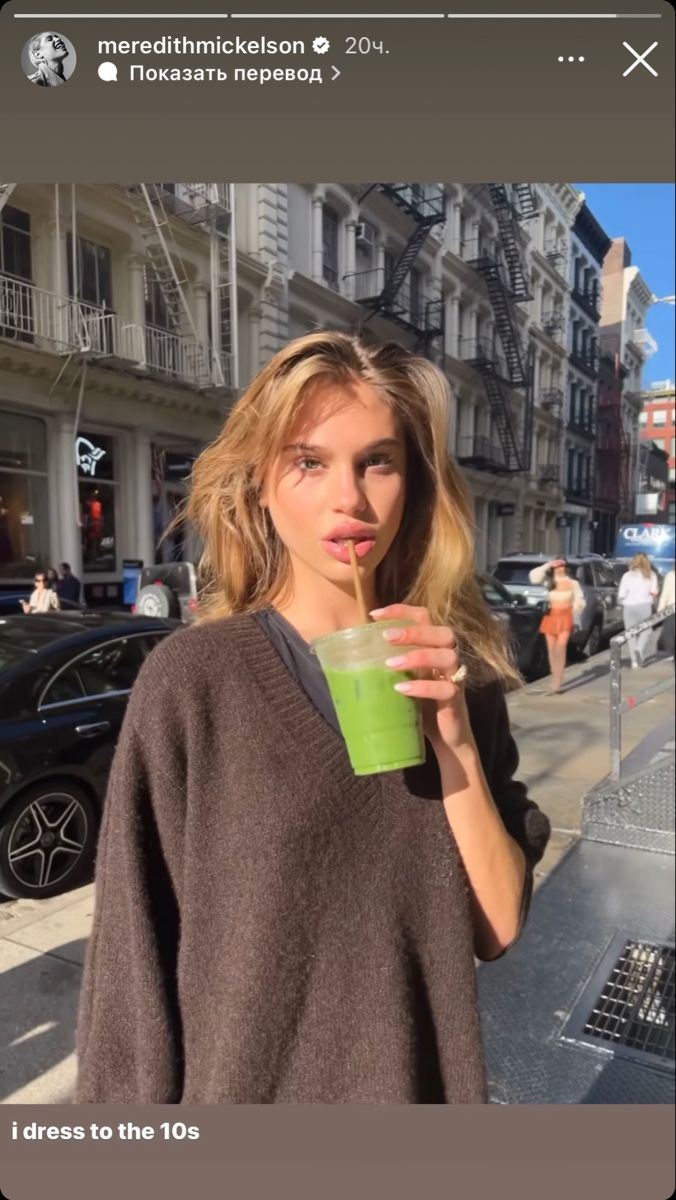 a woman standing on the sidewalk drinking from a green cup