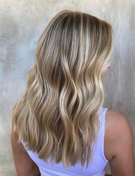 a woman with long blonde hair is looking at the back of her head and wearing a white tank top