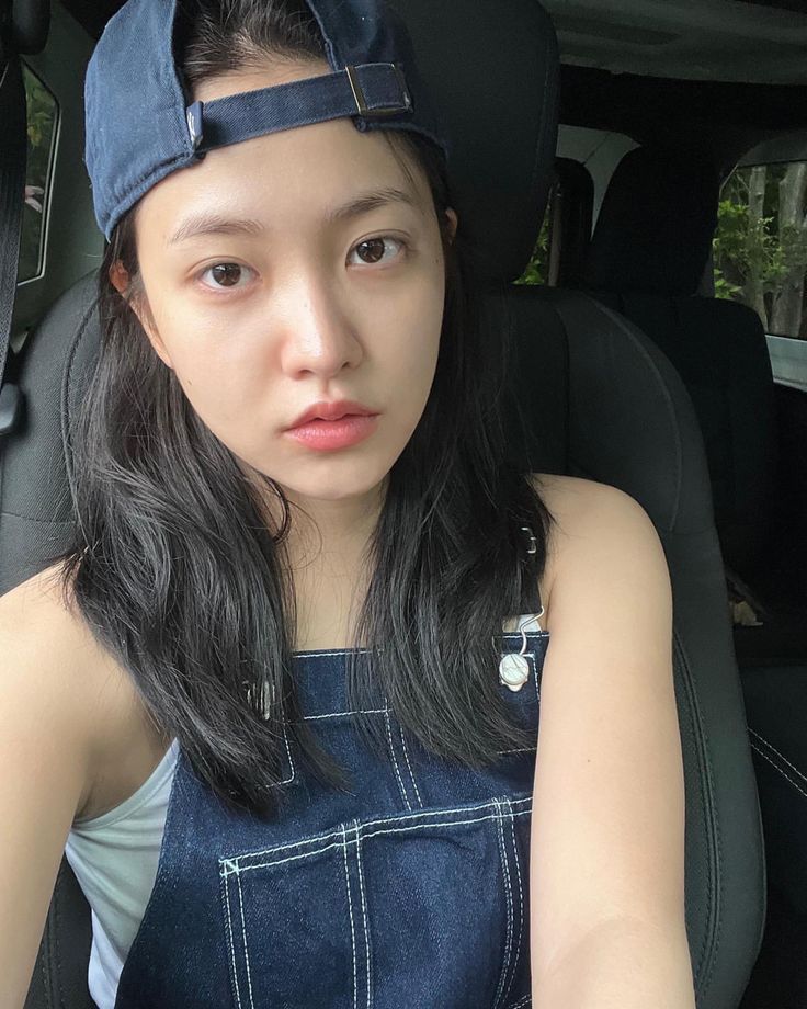 a woman sitting in the back seat of a car wearing a denim dress and cap