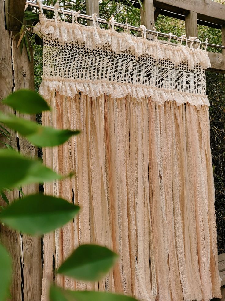 an old fashioned curtain hanging on a wooden fence in front of some bushes and trees