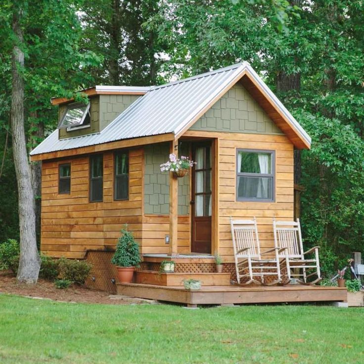 a small wooden cabin in the woods with rocking chairs on the front porch and steps leading up to it