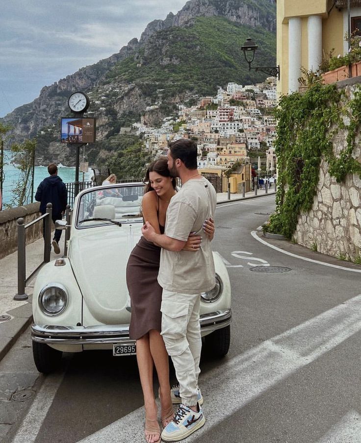 a man and woman embracing in front of a car on the road next to an ocean