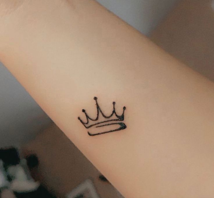 a small crown tattoo on the wrist is shown in black ink, and it appears to be an arrow