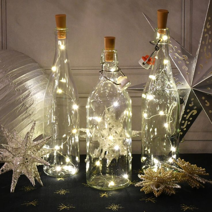 three bottles with lights in them sitting on a table next to an ornament