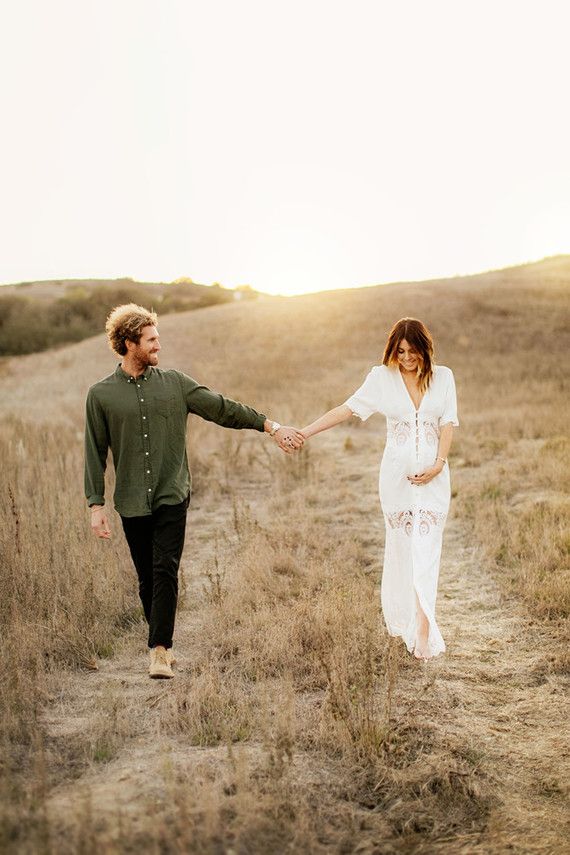 a man and woman holding hands while walking through a field