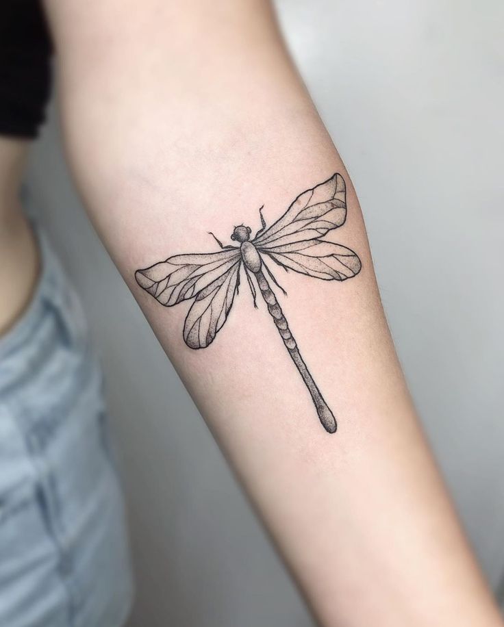 a woman's arm with a tattoo of a dragonfly on the left forearm