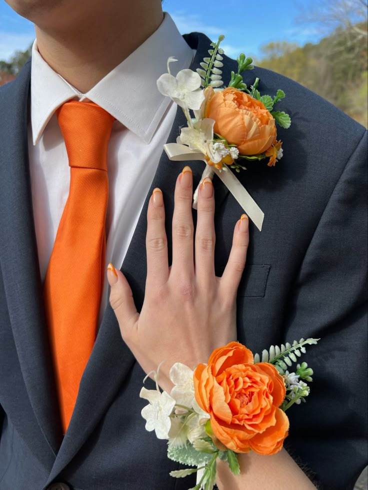 a man wearing an orange tie and matching boutonniere is holding his bride's hand