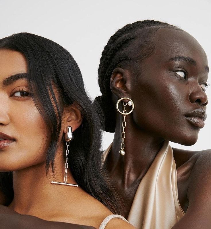 two women wearing earrings and one is looking off to the side with her hand on her shoulder